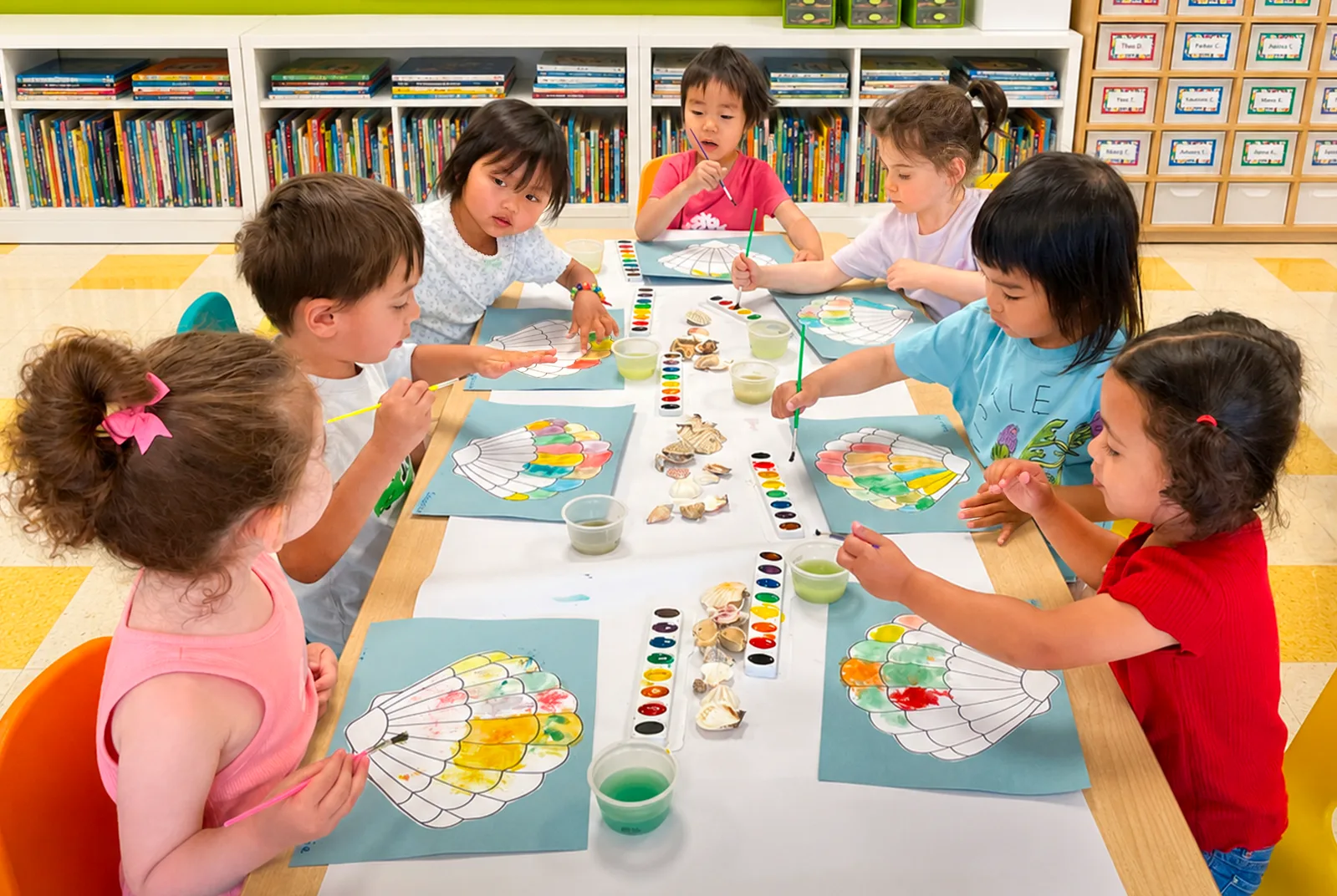 Eight Starbright students around one long table, painting watercolour seashell pictures with real shells laid out between them