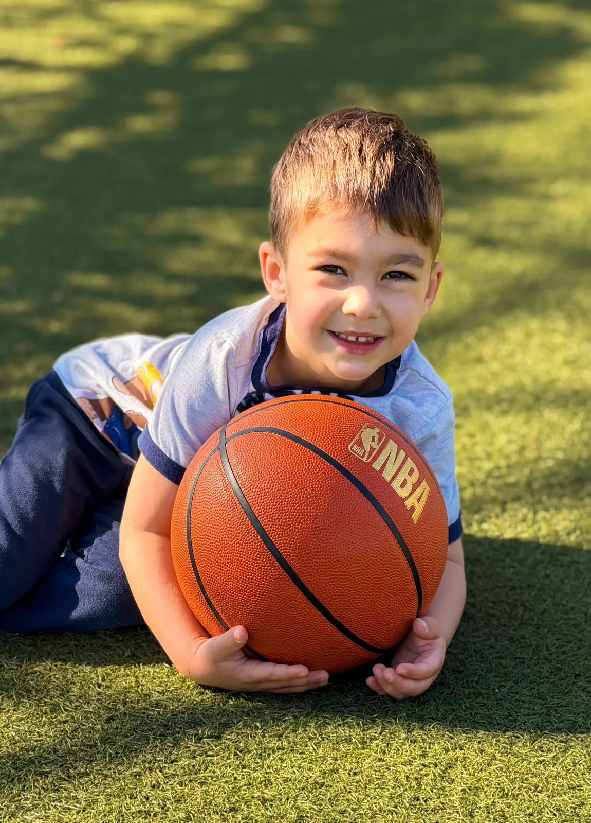 A Starbright preschooler lying on the grass holding a basketball