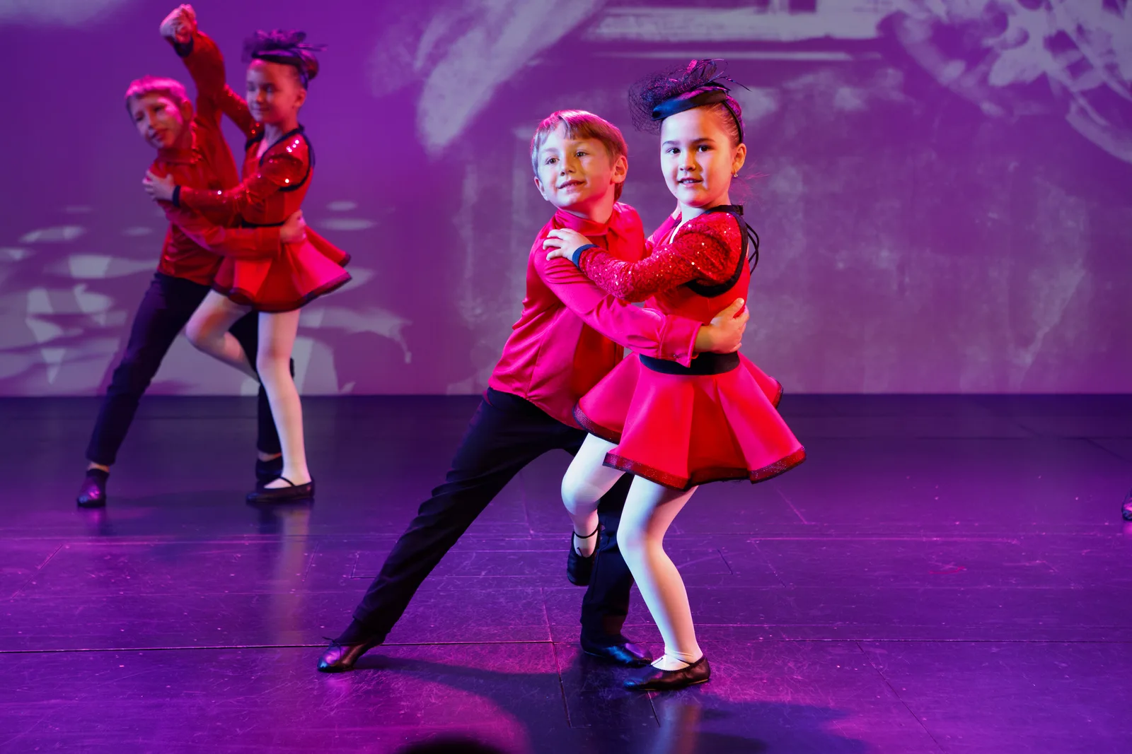 Four Starbright students in red costumes dancing in pairs on the Starbright Theater stage under coloured lights