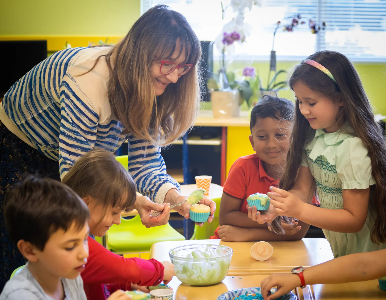A Starbright teacher decorating cupcakes at a classroom table with a group of young children