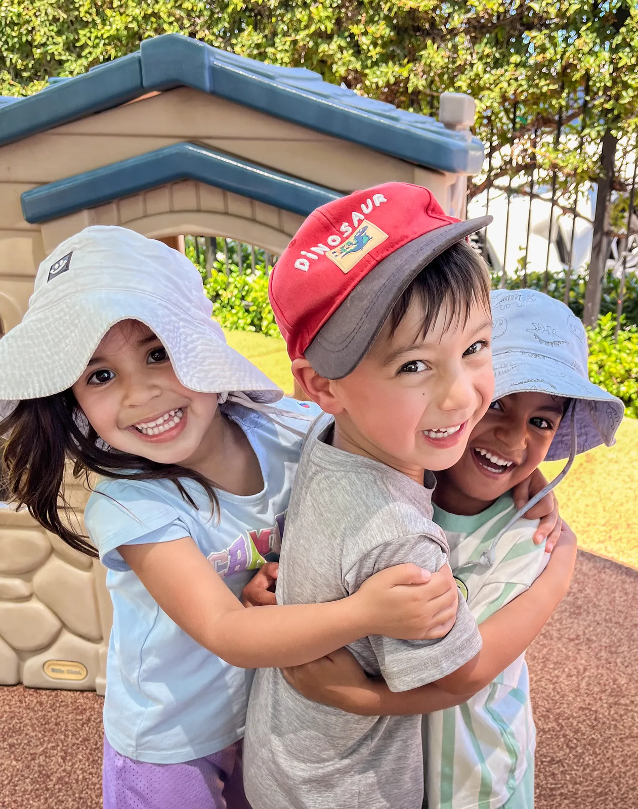 Three Starbright children in sun hats hugging and laughing together on the playground