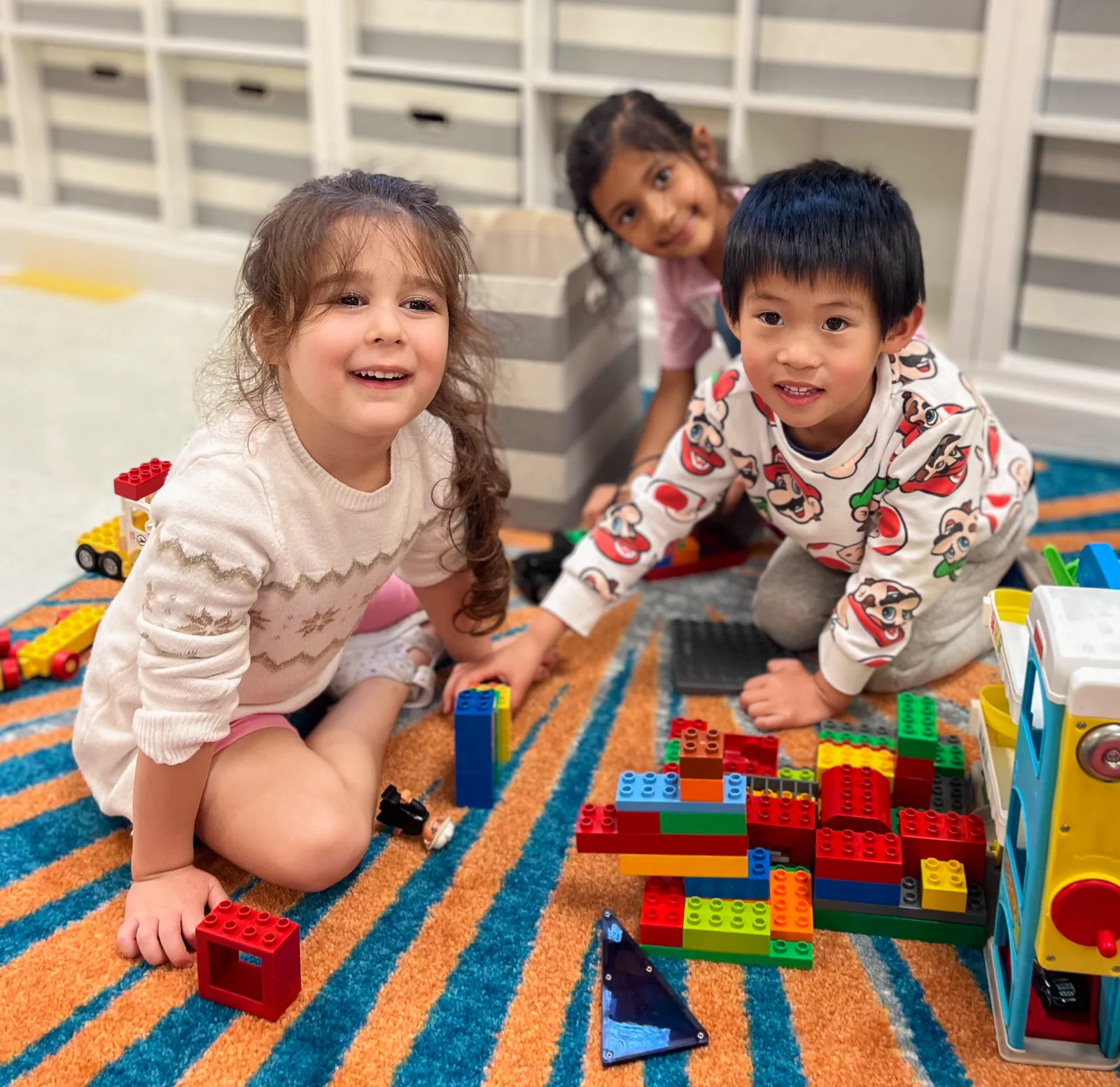 Three Starbright children building with bricks on a classroom rug