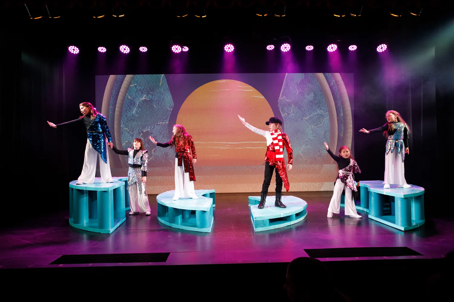 Starbright students performing on geometric set pieces under purple stage lights