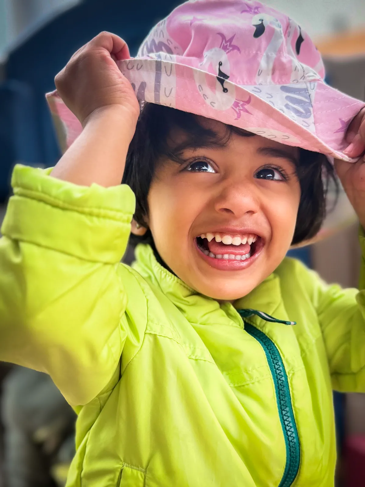 A laughing Starbright toddler in a pink sun hat and bright green jacket, outdoors on a sunny day